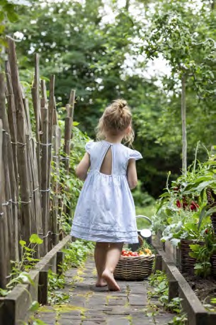 Mädchen im weißen Kleid trägt einen Erntekorb durch einen Tomaten-Tunnel